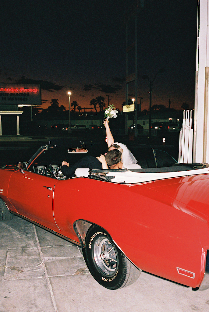 bride and groom celebrating in red convertible