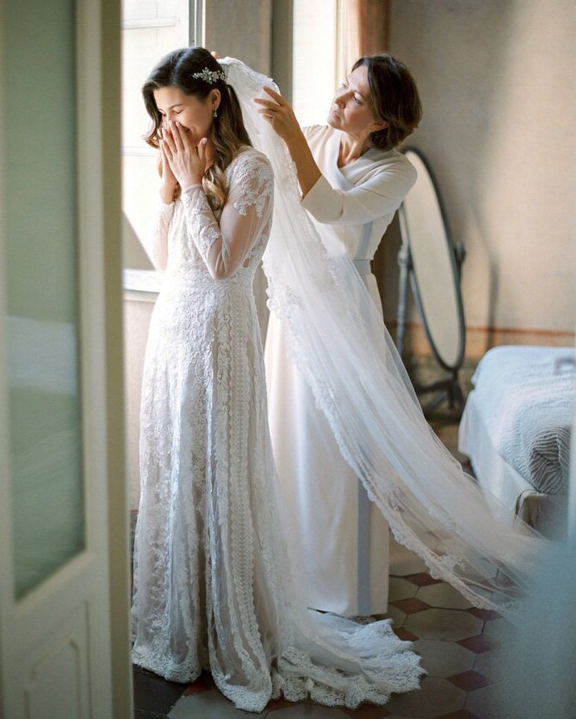 Bride smiling covering her face while mom clips in veil