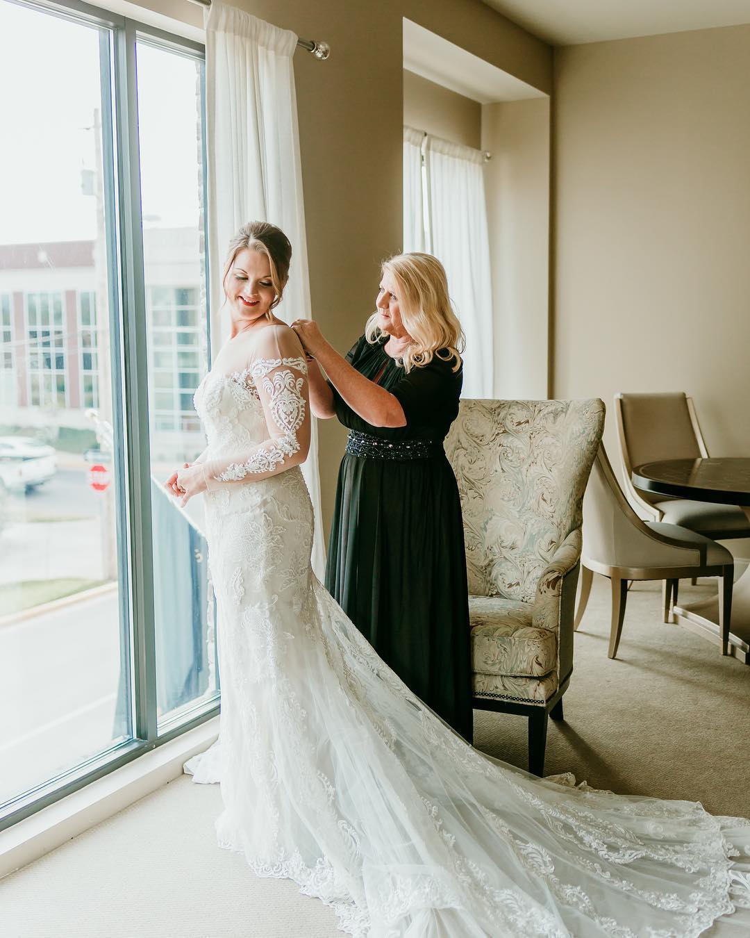 Bride in long sleeve wedding dress while mom secures zipper