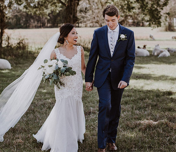 Bride with white bouquet and groom in a pasture