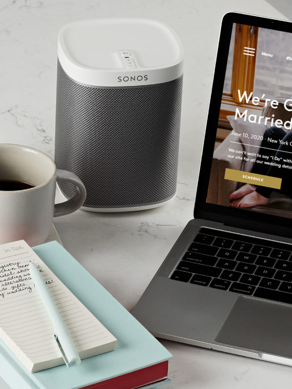 desk set up with pencil holder, mug, notebook, speaker and laptop displaying a wedding website