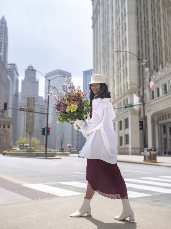 girl walking downtown holding flowers in bridesmaids dress with white dress shirt as a way to restyle a wedding day look