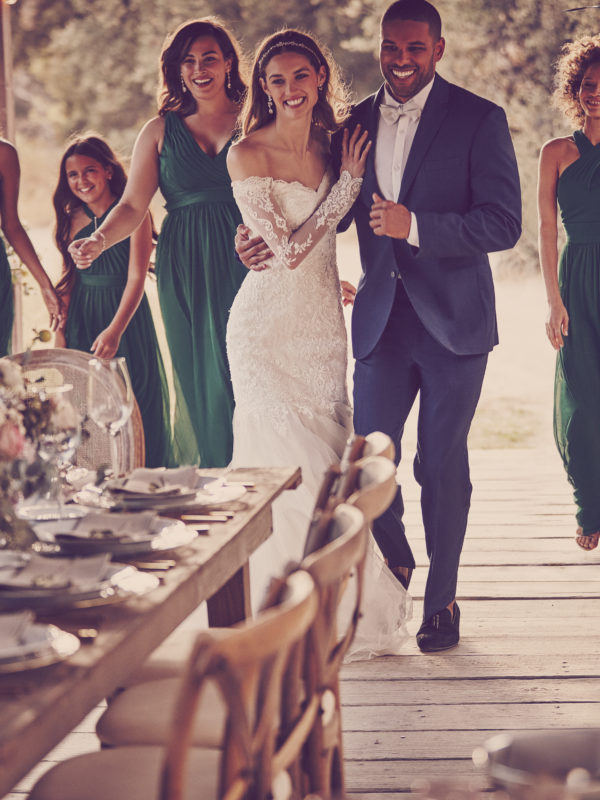 Women and man on walking on covered bridge towards a formal outdoor wedding