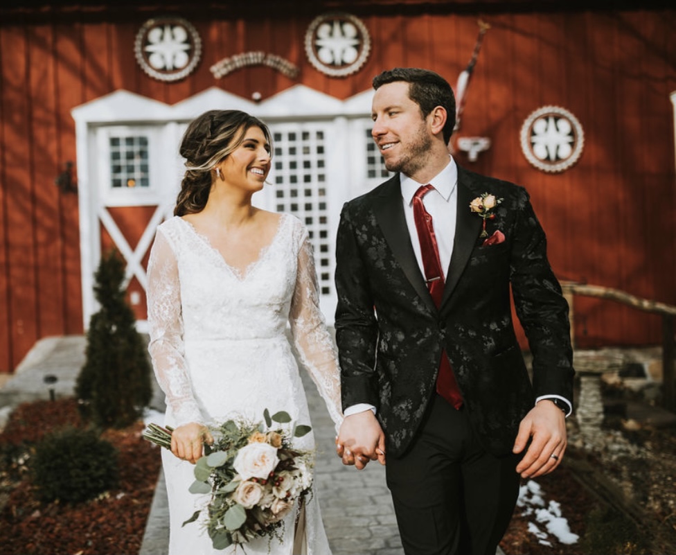 Bride and groom holding hands in front of red barn