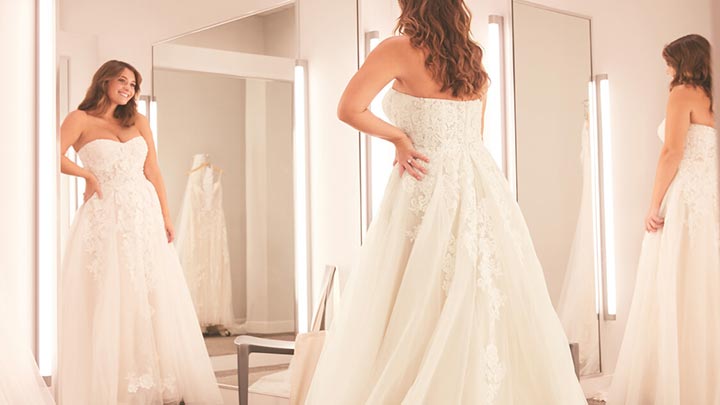 bride in a wedding dress standing in front of a mirror in a store